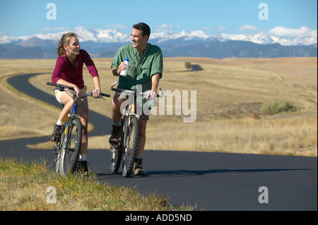 smiling Middle aged couple riding bikes on a trail with mountain range in the background Stock Photo