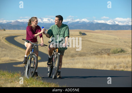Smiling Middle aged couple riding bikes on a trail with mountain range in the background Stock Photo