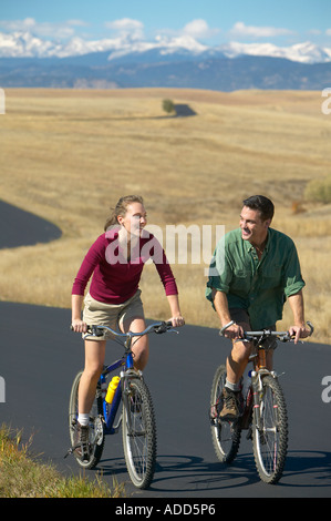 Middle aged couple riding bikes on a trail with mountain range in the background Stock Photo