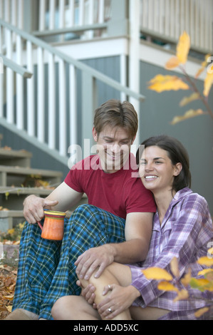 Caucasian couple sitting outdoors with coffee in pajamas in autumn Stock Photo