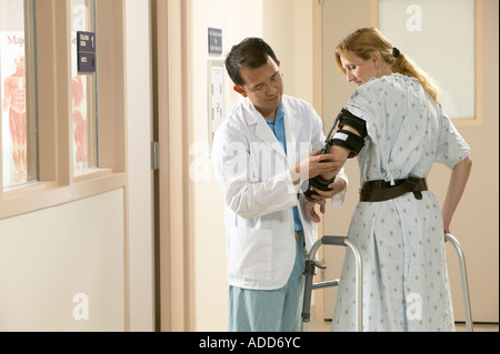 Rehabilitation therapist examines arm brace on female patient in hospital setting Stock Photo
