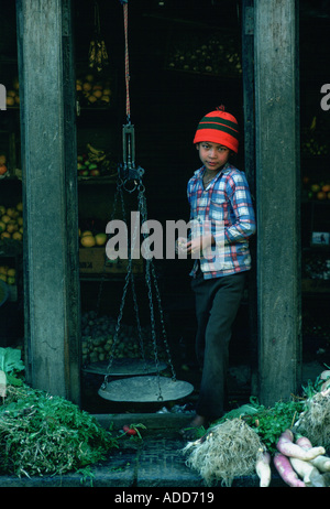 Young boy shopkeeper in fruit and vegetables shop in Patan Nepal uses old fashioned scales Stock Photo