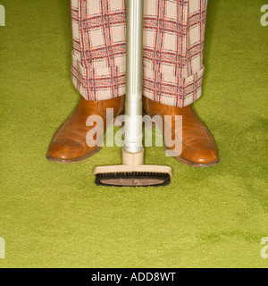 Close up of Caucasian male legs in plaid pants with vacuum extension standing on green retro carpet Stock Photo