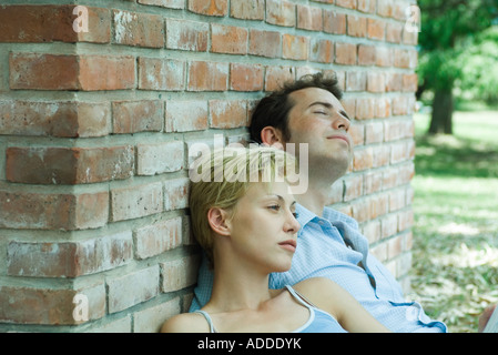 Couple sitting outdoors, leaning against brick wall Stock Photo