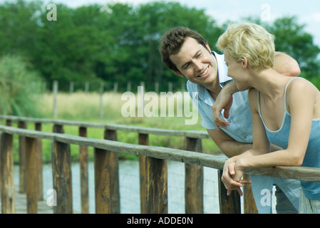 Couple standing on footbridge, leaning against rail, talking Stock Photo