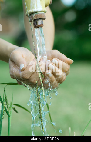 Woman cupping hands under outdoor faucet, close-up, cropped view of hands Stock Photo