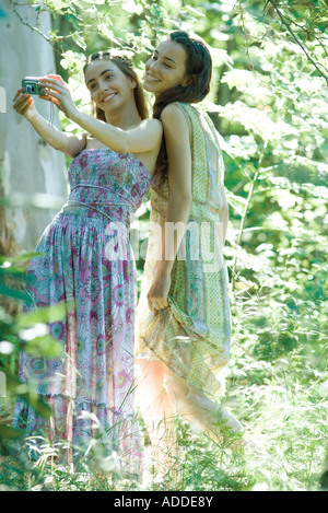 Two young women wearing sundresses, standing in forest, taking photo of selves with digital camera Stock Photo