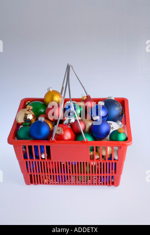 Blurred colorful Christmas tree bulb ornaments piled in red shopping basket with candy canes on white background studio portrait Stock Photo