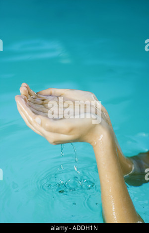 Young woman holding up cupped hands full of water, cropped view Stock Photo