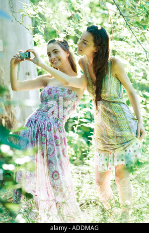 Two young women wearing sun dresses, standing in forest, taking photo with digital camera Stock Photo