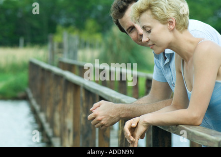 Couple standing on footbridge, leaning against rail, talking Stock Photo