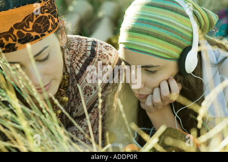 Two young women lying in field, one listening to headphones, close-up Stock Photo