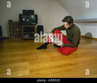 Man sitting on the wooden floor at home and reading a book Stock Photo