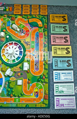 'The Game of Life' by Milton Bradley. The game board & all its' pieces, such as the money & cards, are all spread out.