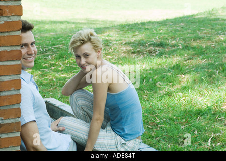 Couple sitting outdoors, next to brick wall, smiling at camera Stock Photo