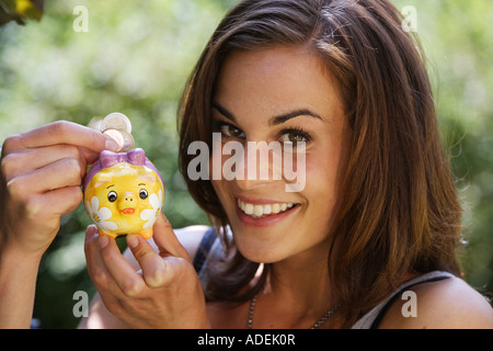 Young woman puts money into a piggy bank © Peter Schatz/Alamy Stock Photo