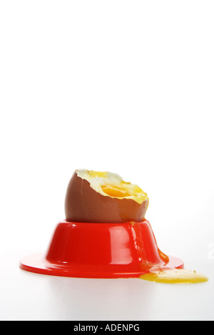 A boiled egg with its shell broken with egg overflowing a bright red egg cup holder against white background Stock Photo