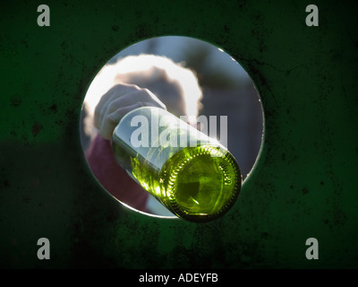 Green Glass Bottle Recycling Bin with grey haired lady putting green bottle through bin hole from inside. England UK Britain Stock Photo