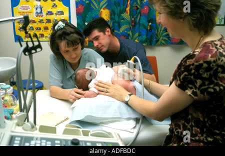 Small newly born baby having a diagnostic ultra sound scan in hospital whilst mother and father look on supportively. Stock Photo