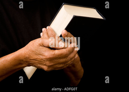 An old woman holds a bible in prayer Stock Photo