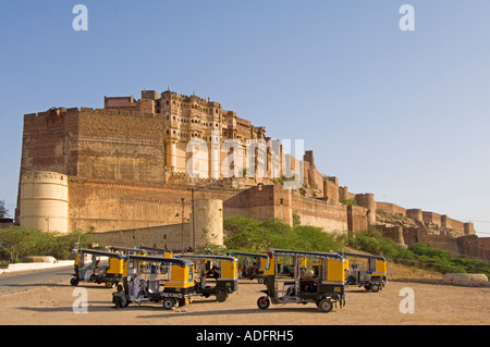 A wide angle view of the Mehrangarh Fort against a blue sky with auto rickshaws in the foreground waiting to take tourists. Stock Photo