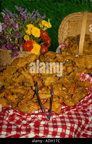 Potluck picnic for July 4th:  Basket of fried chicken on table with red checkered tablecloth and flowers, USA Stock Photo