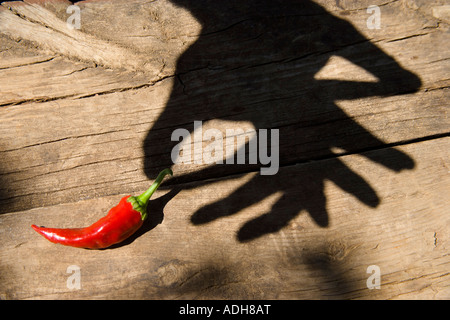 Male hands shadow cast over wooden table as if holding a red pepper Stock Photo