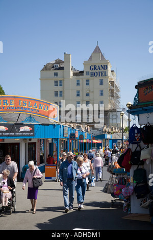 People walking on pier with amusement arcade and stalls in summer with Grand Hotel in background Llandudno Wales UK Stock Photo
