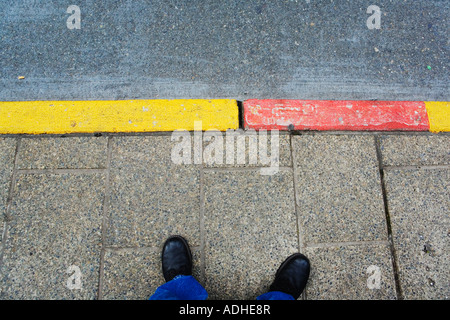 Feet and bus stop curb painted red and yellow Stock Photo