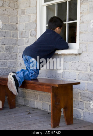 Boy peering through window of building Stock Photo