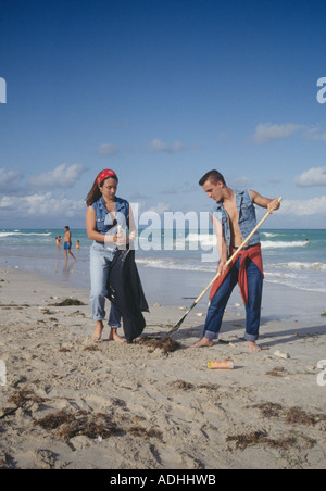 Teenage volunteers dressed in jeans raking trash into plastic bags on Miami Florida Beach