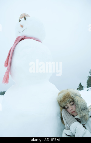 Teen girl resting head against snowman Stock Photo