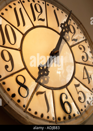 Big oldfashioned clock with shiny glass face with light inside and black numbers with dark metal hands Stock Photo