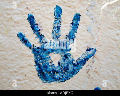 'Silhouette of child's hand covered in blue paint on white wall'. Stock Photo