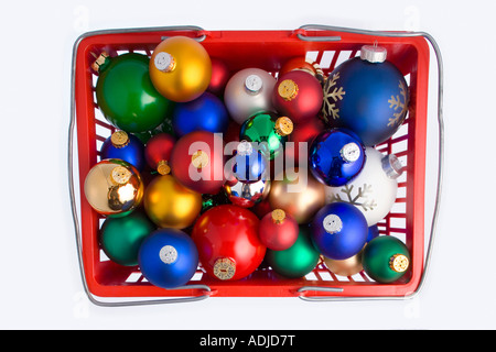 Looking down on a colorful Christmas tree bulb ornaments piled in red shopping basket on white background studio portrait Stock Photo