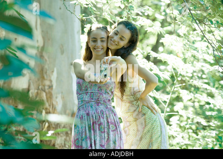 Two young women wearing sundresses, standing in forest, taking photo of selves with digital camera Stock Photo