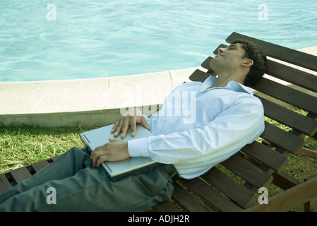 Businessman reclining in lounge chair near pool, holding laptop on lap Stock Photo