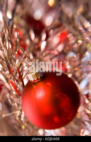 Red Christmas ball hung on tinsel tree branch by paperclip Stock Photo