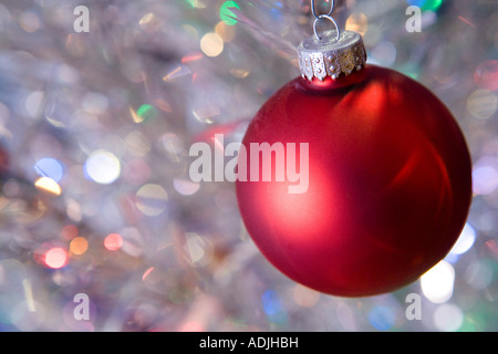 Red Christmas ball hanging from tinsel tree branch by paperclip Stock Photo