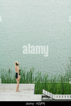 Woman in swimsuit standing on deck, looking towards body of water Stock Photo