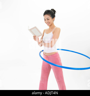 A woman is doing hula hoop and reading a book Stock Photo