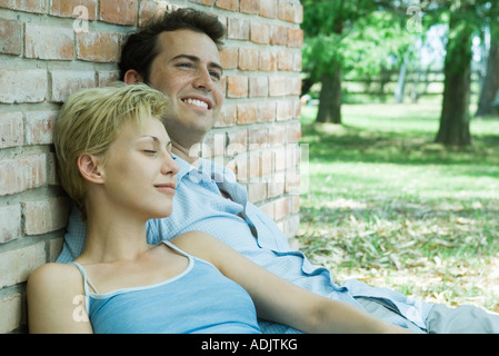 Couple sitting, leaning against brick wall Stock Photo