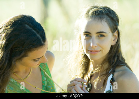 Two young women outdoors in sun, one holding the other's necklace Stock Photo