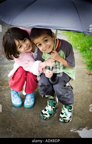 Brother and sister shelter together under umbrella Stock Photo