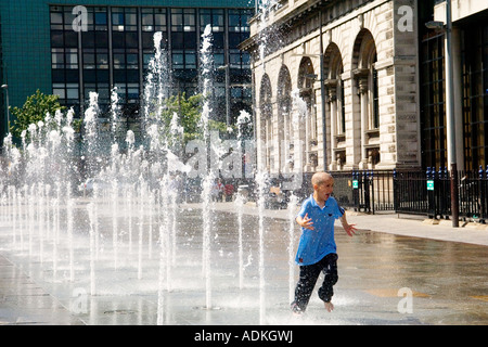 Donegall Quay, Belfast, County Antrim, Northern Ireland. Boy running through Queens Square fountain beside the Custom House. Stock Photo