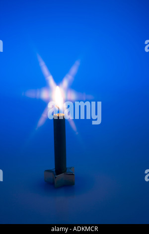 One gold Chirstmas candle lit with star base on dark blue background studio portrait Stock Photo
