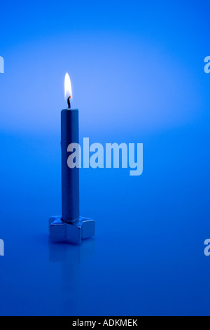 One gold Chirstmas candle lit with star base on dark blue background studio portrait Stock Photo