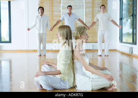 Group therapy, two women sitting back to back while three adults hold hands in background Stock Photo