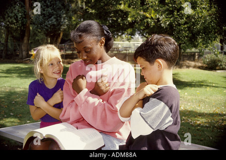 multicultural Two young children learning  'love' ASL sign language  african american teenage girl reads reading from Bible United States Myrleen Pearson Stock Photo