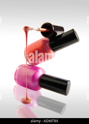 2 Nail Polish bottles balanced on each other in a fun way with a nail varnish brush balanced ontop dripping nail varnish Stock Photo